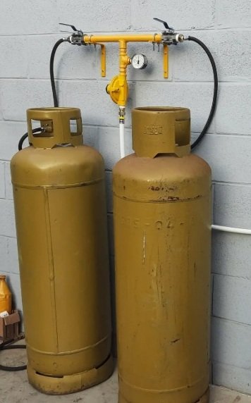 Dois cilindros de gás amarelos conectados a um sistema com válvulas e manômetro em uma parede de concreto