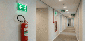 Extintor de incêndio e placas de sinalização luminosa em um corredor corporativo, equipamentos essenciais para a emissão do avcb bombeiros.