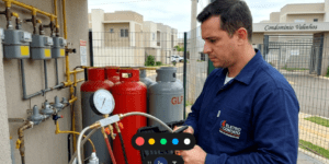 Um técnico da Eletro Contato, uniformizado, verifica um manômetro e usa ferramentas durante um teste de estanqueidade de gás em Valinhos, em uma central de gás de condomínio com cilindros de GLP.