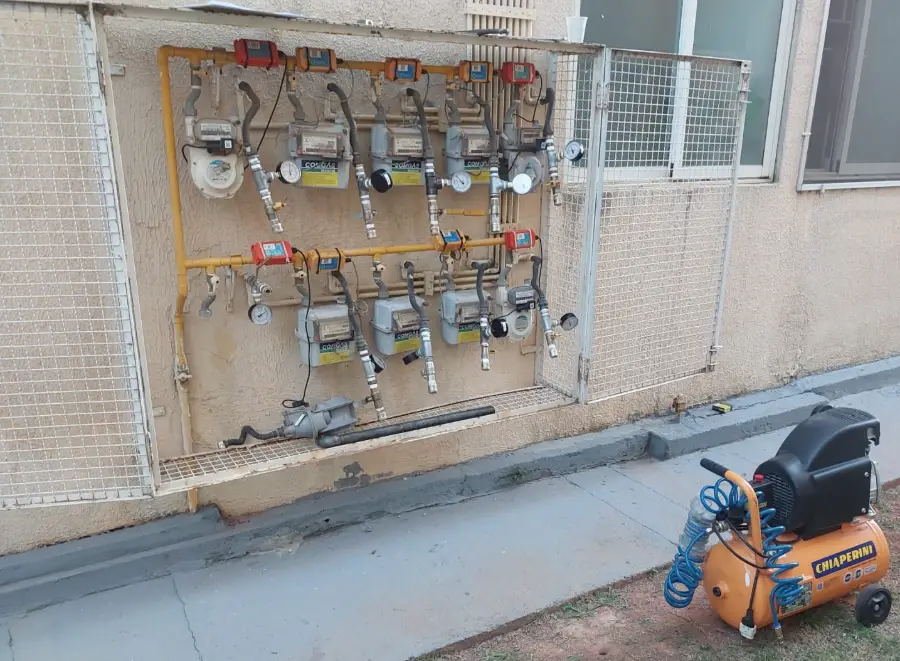 Abrigo de medidores de gás de condomínio com manômetro instalado em cada ramal durante teste de estanqueidade, compressor ao lado